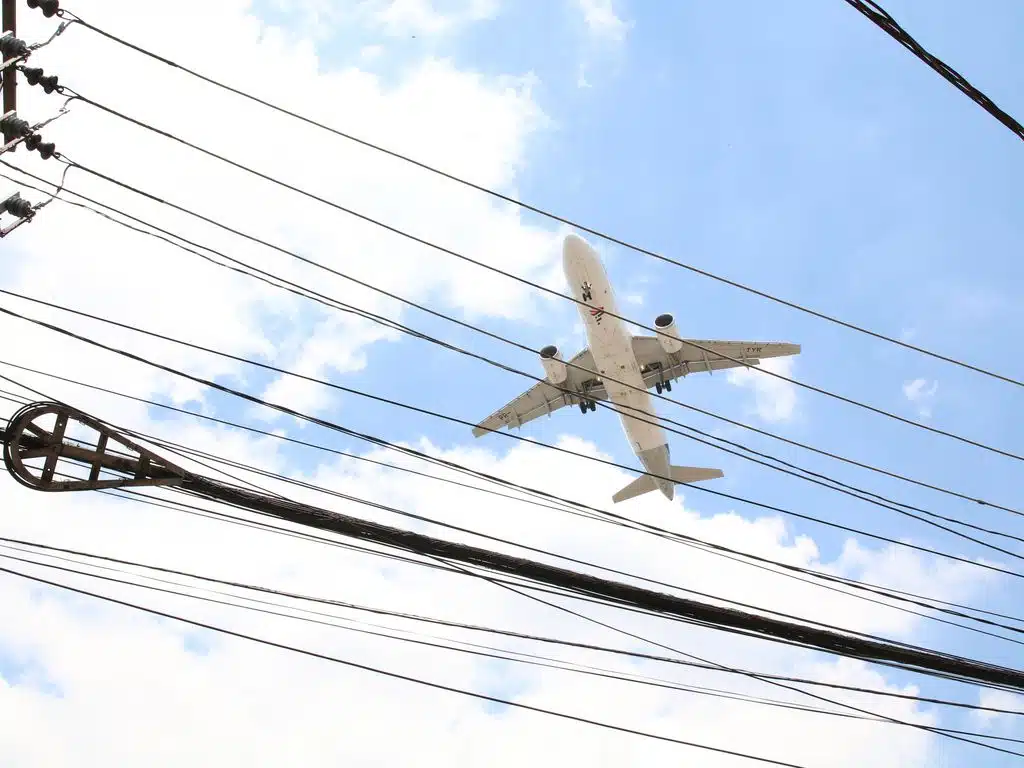 Avião sobrevoa bairro em São Paulo . No primeiro plano aparecem fios da rede elétrica.