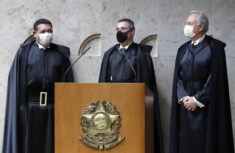 Ministro Cássio Nunes Marques à esquerda, André Mendonça no Centro e Ricardo Lewandowski à direira. Todos usam a toga, vestimenta na cor preta, longa até perto do chão, com camisa branca por baixo e máscaras de proteção.