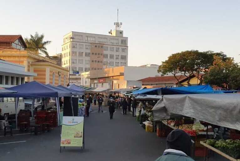 Barracas de feira montadas em rua de Amparo. Pessoas caminham pelo local.