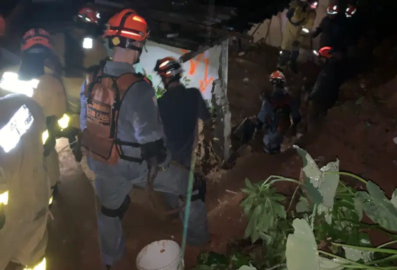 Bombeiros em barranco próximo a casas atingidas por deslizamento de terra.
