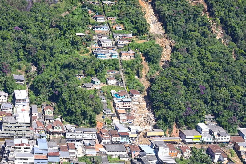 Foto mostra morro com muitas casas e local onde houve deslizamento