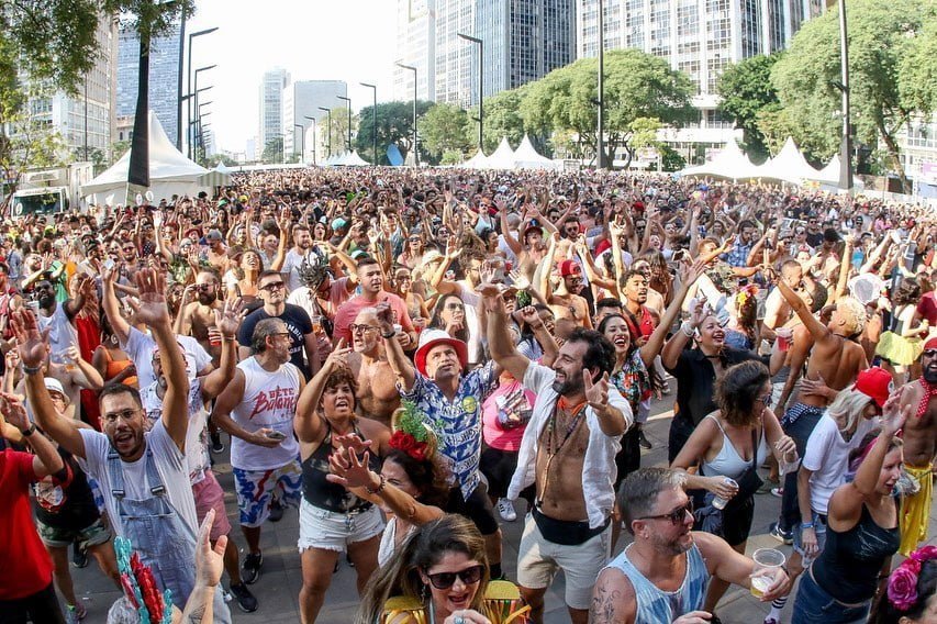 Foto mostra Vale do Anhangabaú tomado por foliões. Alguns estão com as mãos para o auto enquanto cantam e dançam.