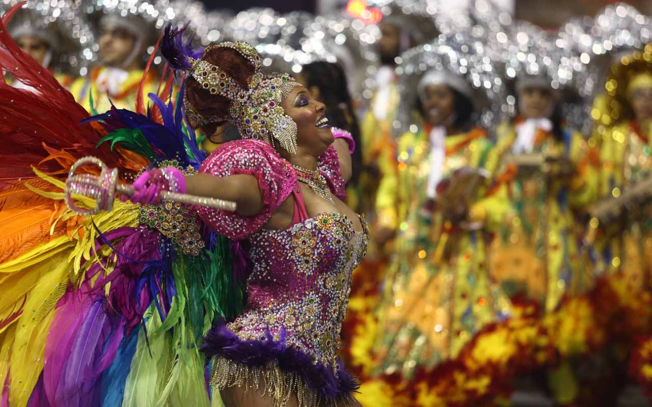 Passista abre os braços enquanto olha para o céu. Ao fundo, outros integrantes da escola de samba.