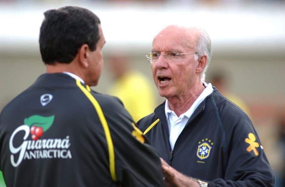 Zagallo com uniforme da seleção conversa com Parreira, que aparece de costas na foto. Nas costas de Parreira há o nome do Guaraná Antárctica.