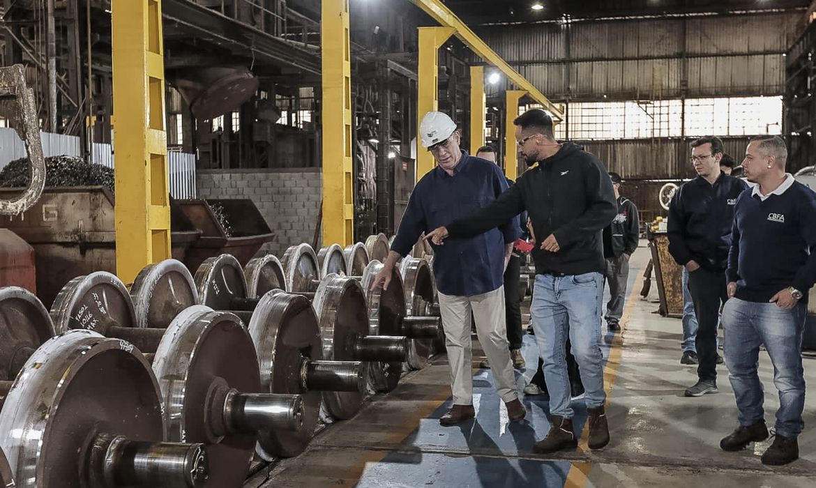 Com capacete de proteção, ciro gomes visita fábrica. Funcionário mostra o local apontando o dedo. Outras pessoas acompanham.