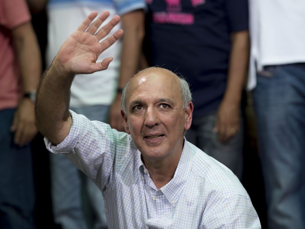 José Roberto Arruda, ex-governador do DF, homem de pele clara, careca - com cabelo na lateral da cabeça, cabelos brancos, acena com a mão direita.