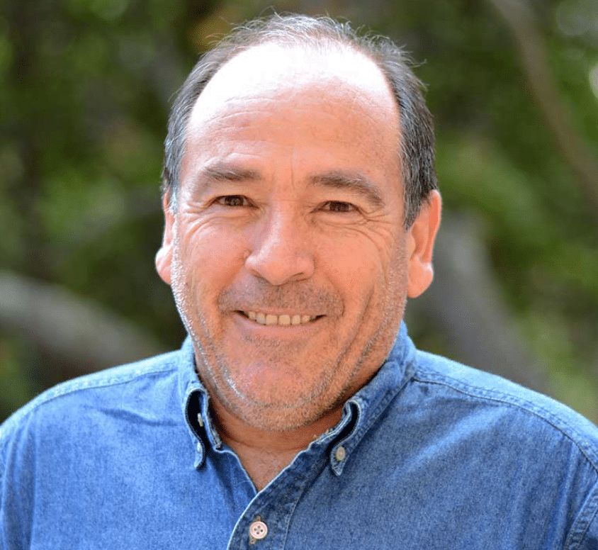 Miguel Altieri, homem de pele clara, sorri para a foto. Ele tem cabelos com fios brancos na lateral da cabeça e é calvo na parte de cima da cabeça.