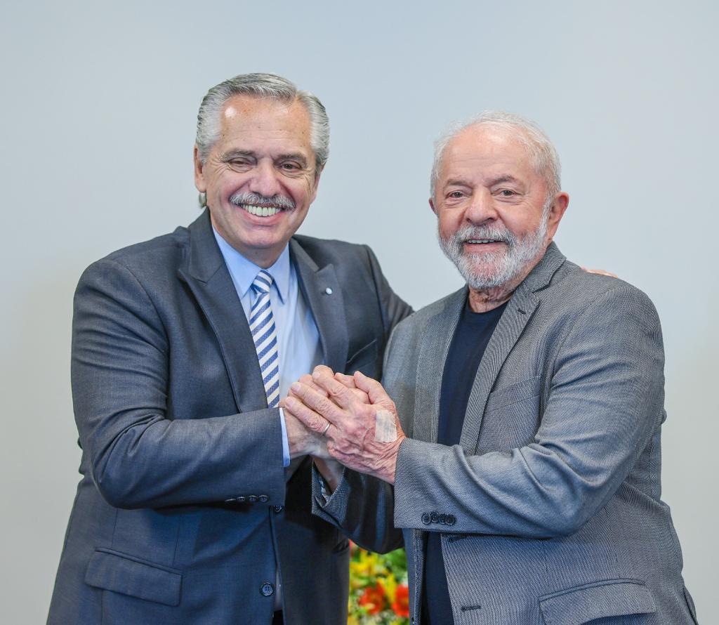 Alberto Fernandez, presidente da Argentina, homem de pele clara, cabelos grisalhos, e Lula, homem de pele clara, calvo na parte do meio da cabeça e cabelos grisalhos na lateral da cabeça. Os dois sorriem para foto enquanto mantêm as mãos dadas.
