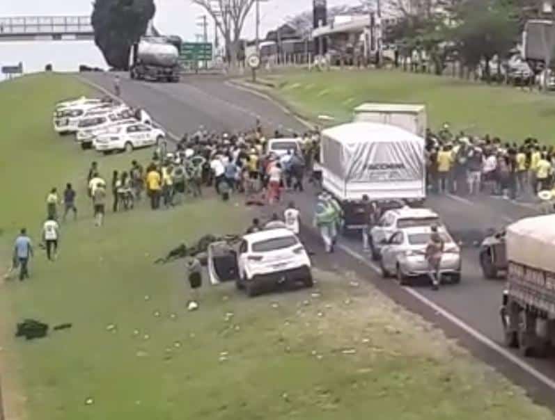 Imagem mostra bolsonaristas fechando rodovia e carro avançando sobre eles. Viaturas da PM aparecem do lado esquerdo da via.