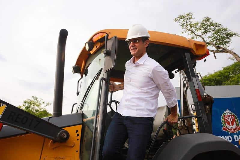 Rodrigo Garcia com capacete na cabeça descendo de um trator. Ele veste camisa social.