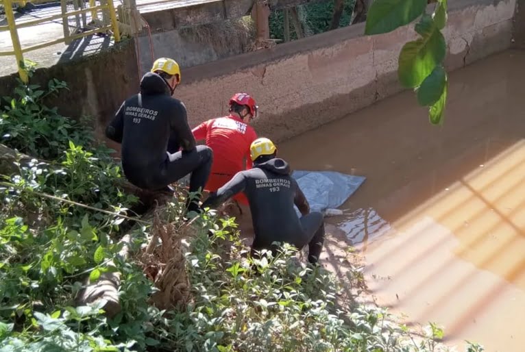 Bombeiros aparecem em canto de córrego ao lado de corpo que aparece coberto com plástico.