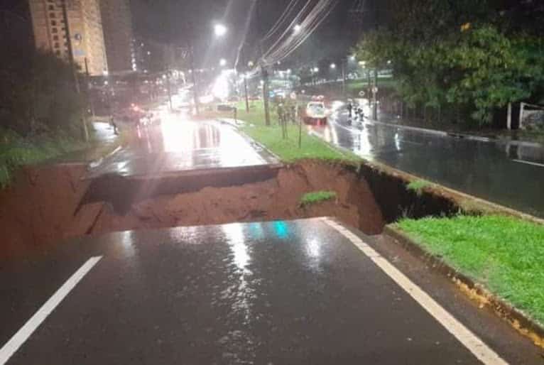 Foto noturna mostra buraco aberto no meio da rua, engolindo todo asfalto.