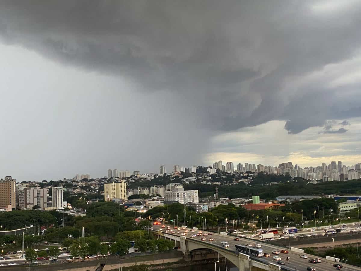 Imagem mostra nuvens carregas se deslocando sobre a cidade de SP. A foto foi feita do alto e mostra ruas e avenidas na parte de baixo, distantes da chuva, enquanto a chuva ai no fundo da cidade, encobrindo parte dos prédios.