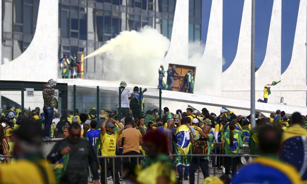 Imagem mostra golpista reunidos em frente a prédio na praça dos três poderes. No alto da foto, na rampa do palácio, homem aciona extintor de incêndio. Fumaça branca cobre parte do local.